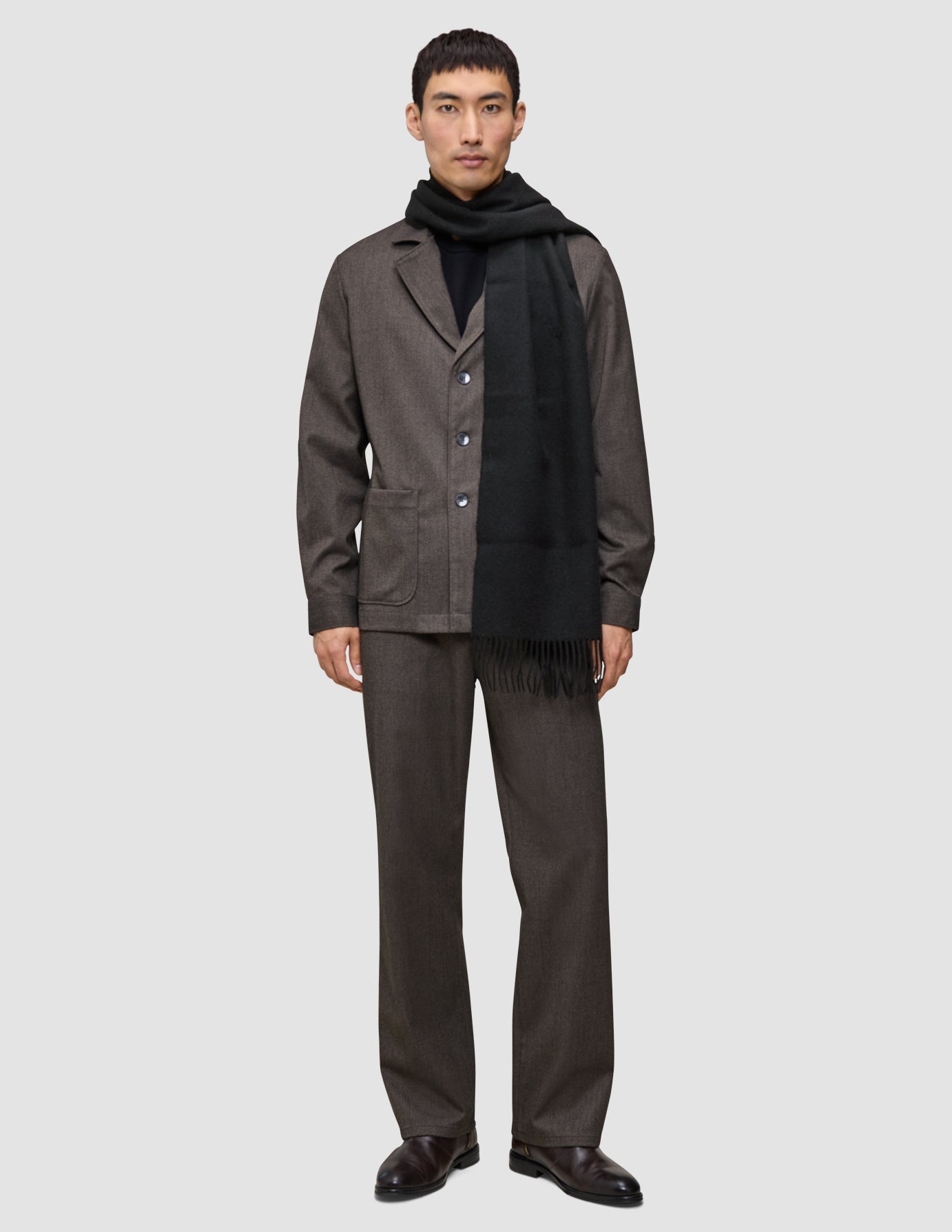 A person wearing a dark brown suit, black turtleneck, and a black wool Scarf Black with fringed ends.